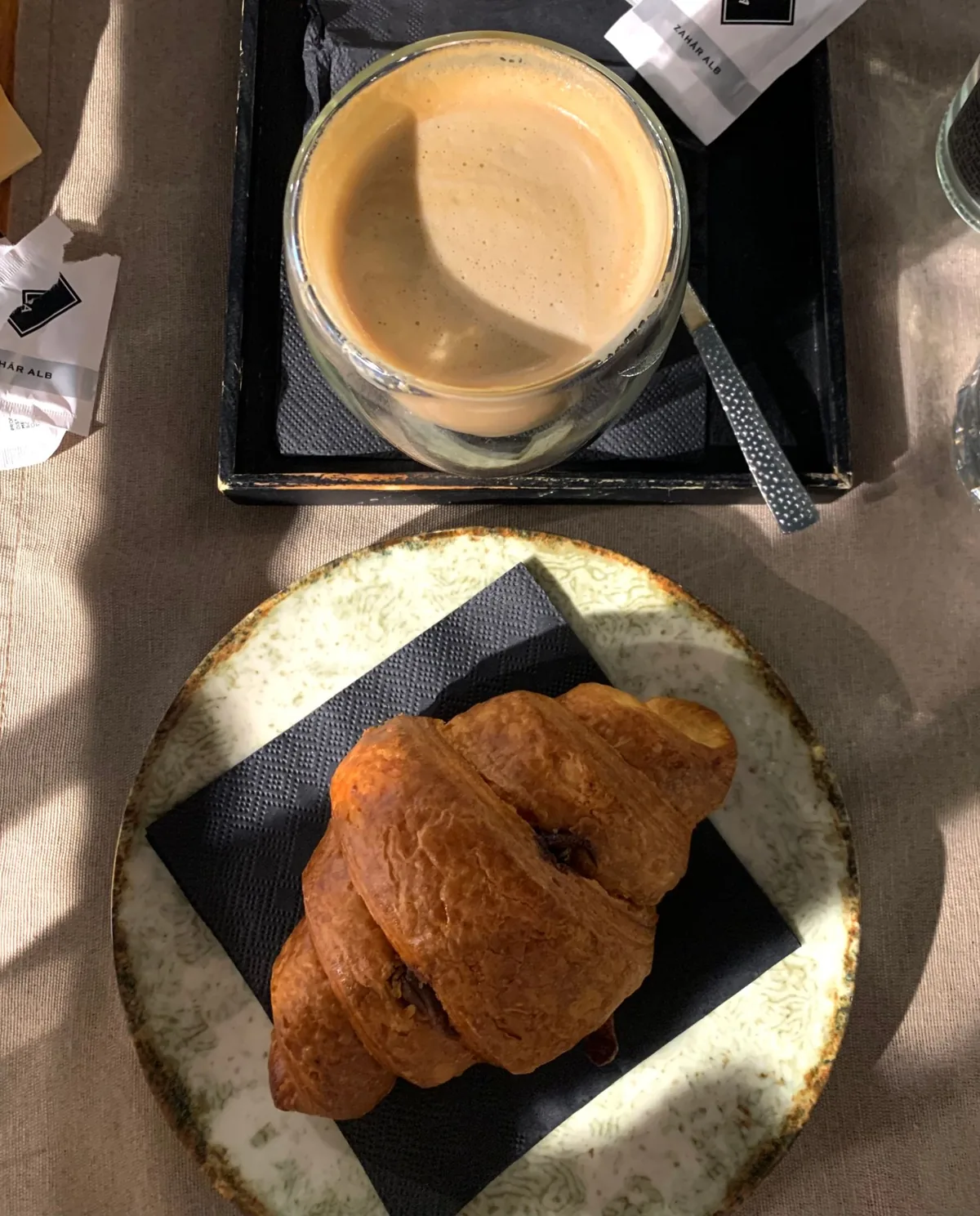 A butter croissant on a ceramic plate beside a coffee