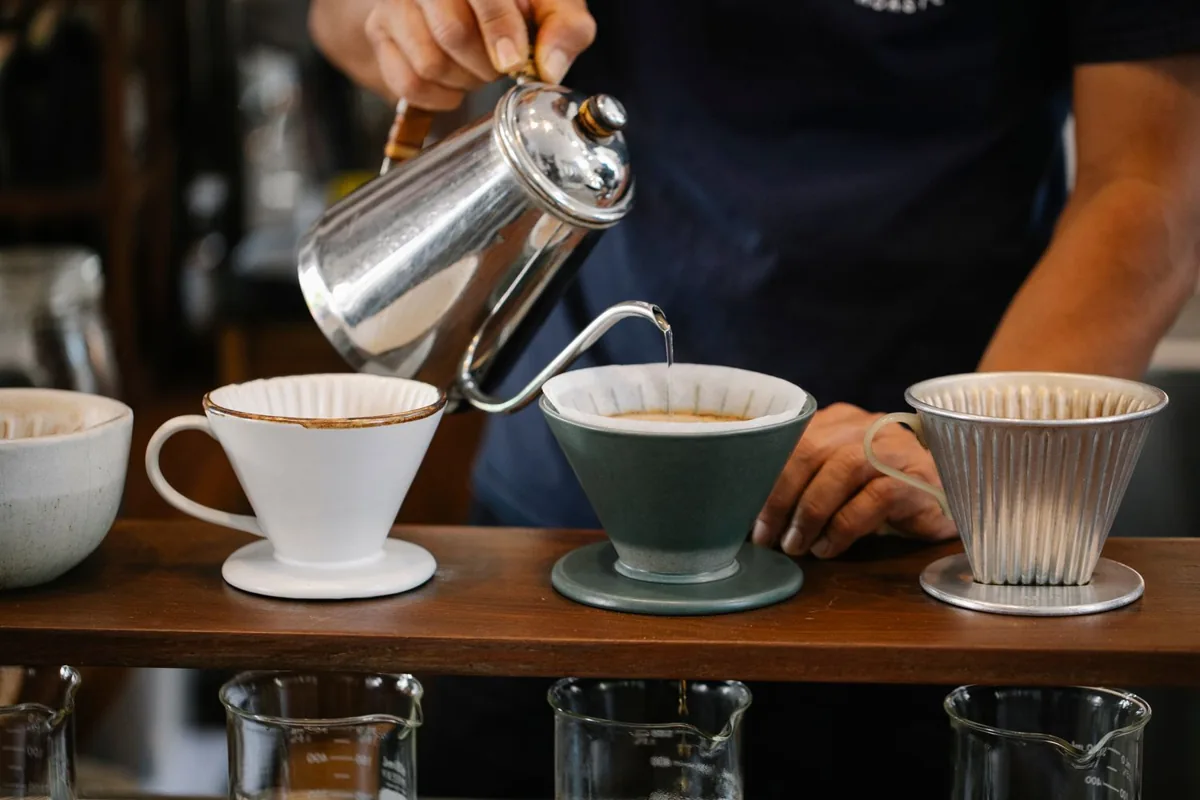 A barista slowly pouring water from a kettle into a ceramic coffee dripper